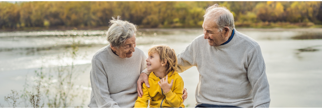 great grandparents with great grandchild sitting by a lake